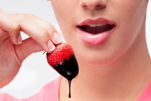 Woman eating a strawberry dipped in chocolate sauce