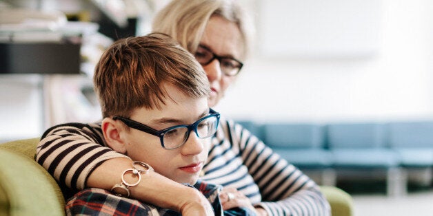 Mature mother with her teenage Son relaxing at home. Both are reading from Tablet computer