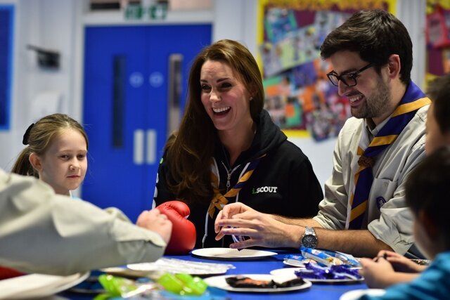 The Duchess of Cambridge sitting beside Scout Leader Carlos Lopez-Plandolit (right), learns about disability by wearing a boxing glove to handle a fork as she meets with children at the newly established 23rd Poplar Beaver Scout Colony in east London. PRESS ASSOCIATION Photo. Picture date: Tuesday December 16, 2014. Kateâs visit supports the Scout Association's 'Better Prepared' campaign, which aims to help communities to deliver Scouting to two hundred locations across the UK where Scouting can have the biggest impact. Photo credit should read: Ben Stansall/PA Wire