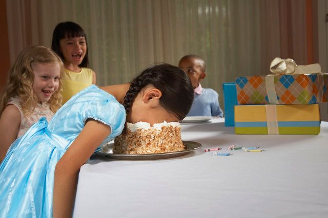 Four children (5-8) at table, laughing at girl with face in cake