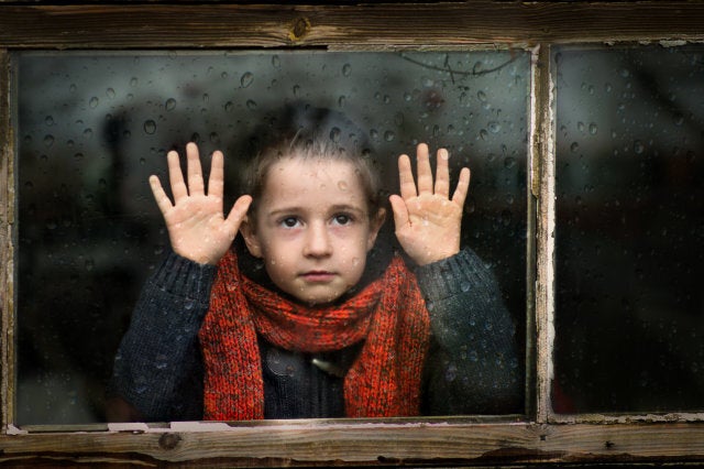 Little boy with red scarf watching through the window