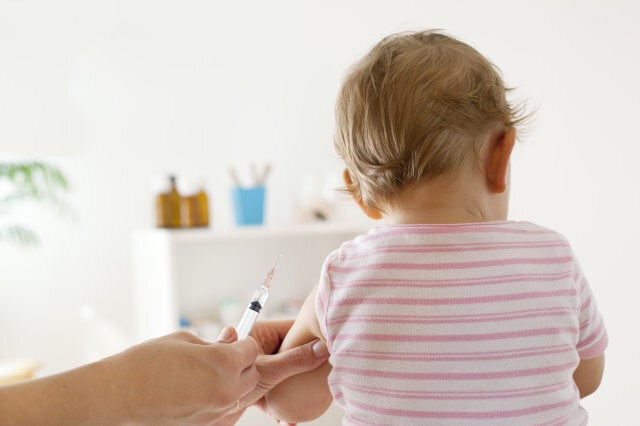 'Bck View of baby girl patient receiving vaccine at the doctor's office, focus on hand holding vaccine'