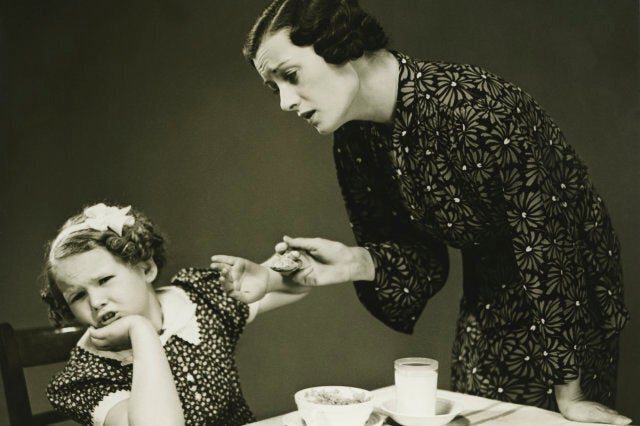 Mother trying to make daughter (4-5) finish food at table, (B&W)