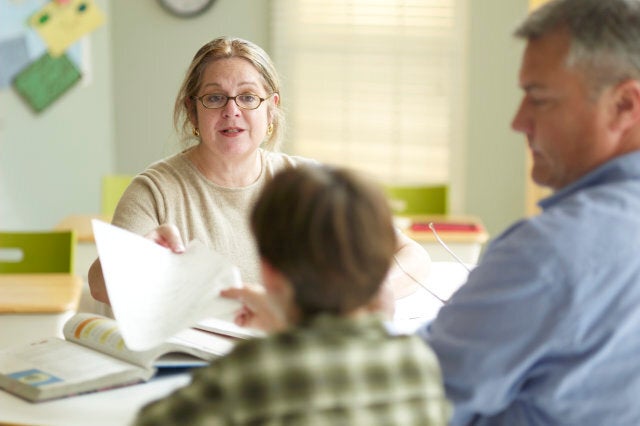 Boy (9-11) with father and female teacher, sitting at desk in classroom