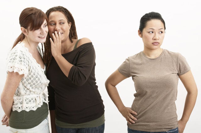 Young woman whispering in friend's ear, looking at young woman