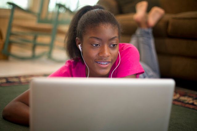 African American teenager with earbuds on computer