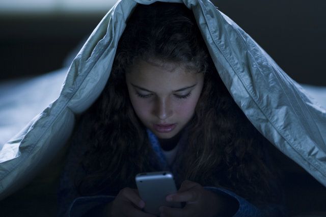 Girl under blankets at night with a smart phone