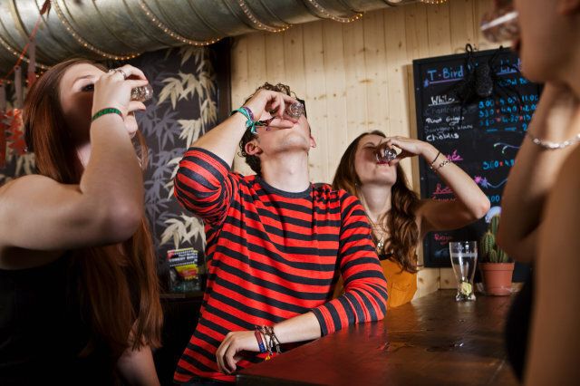 Young friends drinking from shot glass in bar
