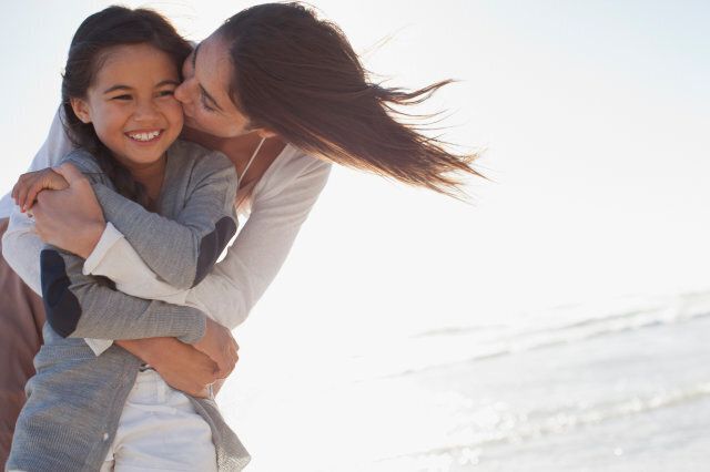 Mother hugging and kissing daughter on beach