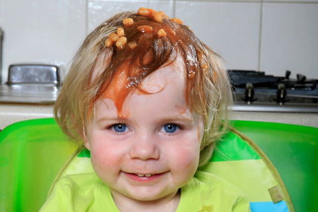 Child with baked beans on head smiling. child eating baked beans child in high chair child in kitchen