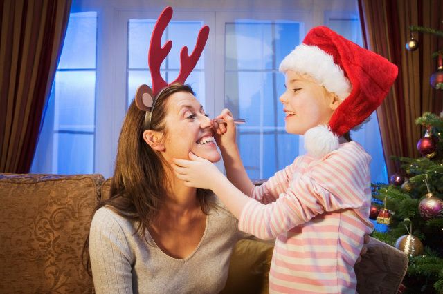 Girl drawing red reindeer nose on mother's face
