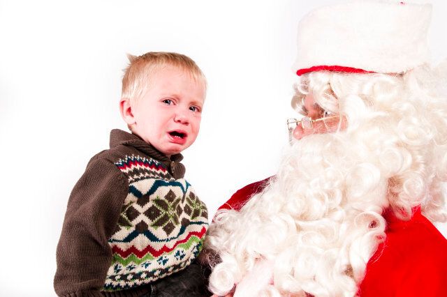 a sad little boy with santa. Santa is looking at the crying boy. Isolated on a white backdrop