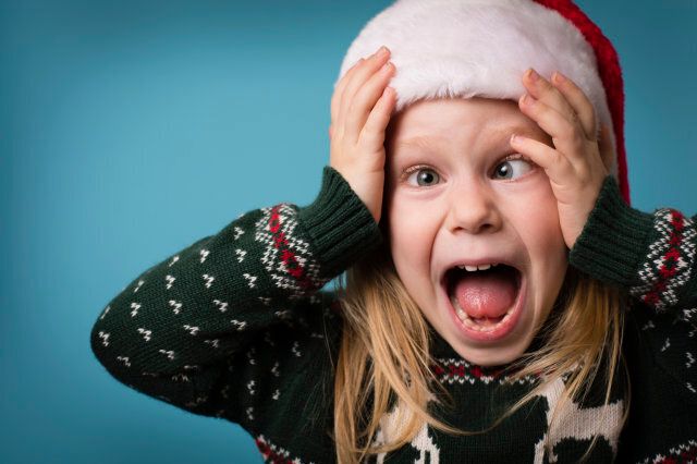 Color image of a little girl wearing a Santa hat and an ugly Christmas sweater, with a stressed/overwhelmed face.