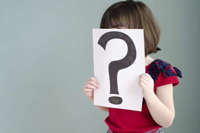 little girl peeks over a sign with a question mark on it