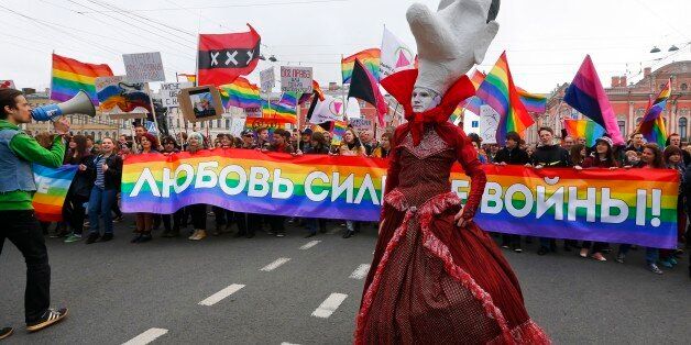 A gay rights activist wearing a mask walks ahead of a squad of gay rights activists, during a tradition May Day rally in St.Petersburg, Russia, Thursday, May 1, 2014. The poster reads : 'Love is stronger than war!'.(AP Photo/Dmitry Lovetsky)