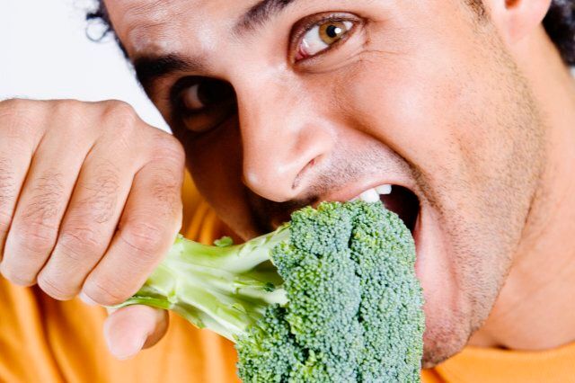 Portrait of a young man eating a broccoli