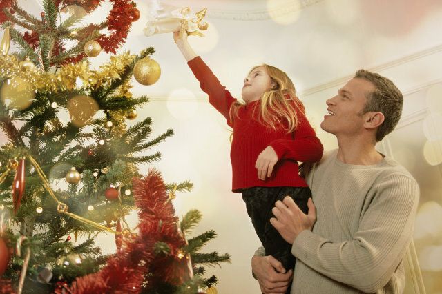 Father helping young daughter place star on top of Christmas tree