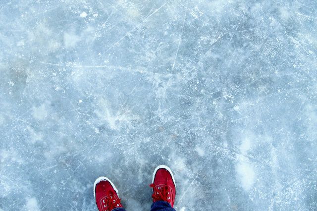 Red shoes standing on thin cracked ice of outdoor rink.