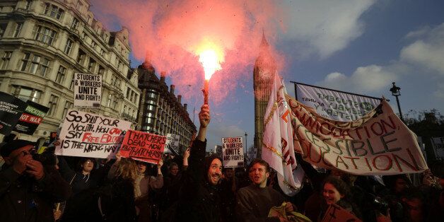 A protestor holds a flare as others parade with banners during a protest against university tuition fees in London, Wednesday, Nov. 19, 2014. University tuition fees nearly trebled four years ago, a move that sparked violent student protests. (AP Photo/Matt Dunham)