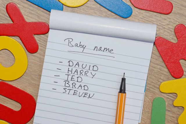 Choosing baby name for a boy written on a note, around wooden letters