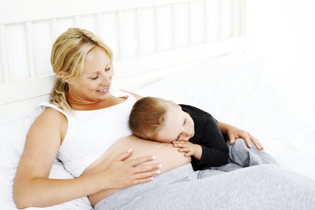 Little boy listening to sounds from the belly of his pregnant mother on a bed at home