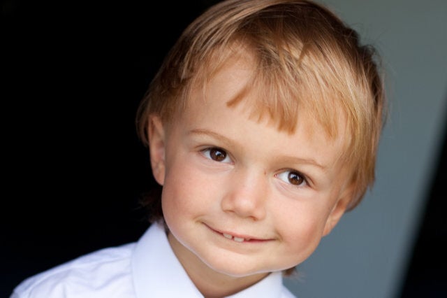 Little boy is smiling happily before his first day at school wearing uniform including tie.