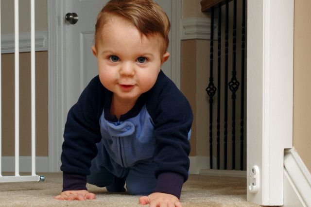 A 6-month old baby boy crawls around a safety gate and is approaching the top of the stairs.