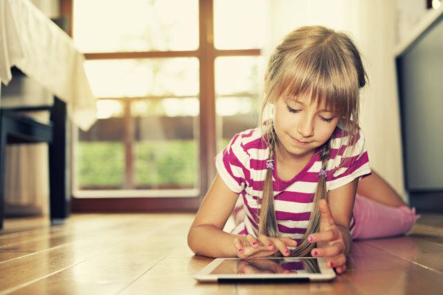 Smiling little girl using tablet on the floor.