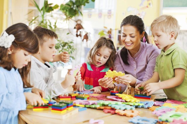 Group of kids playing together with their young nursery teacher.