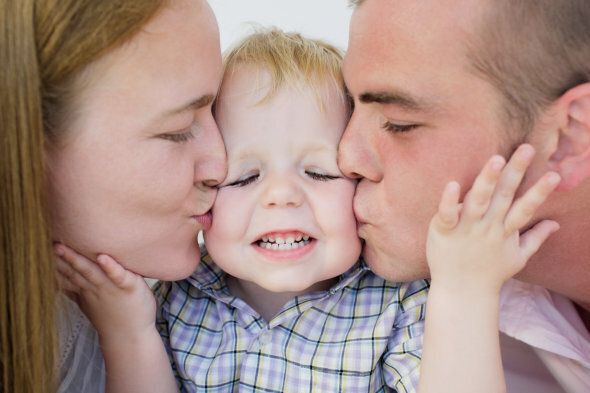 A young couple kissing the cheeks of a baby boy, smiling