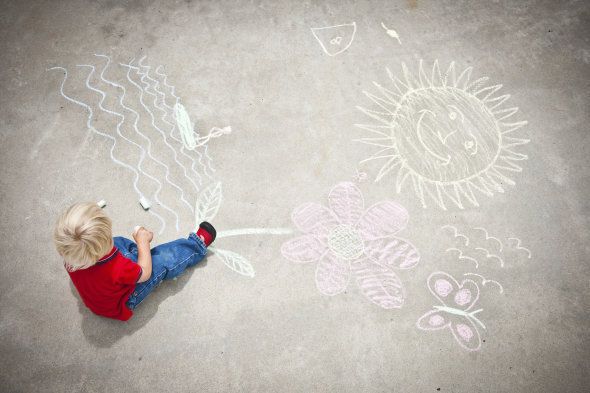 A little boy drawing with chalk on the sidewalk.