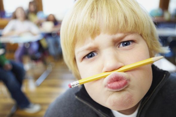 School boy balancing a pencil on nose with classroom at the back