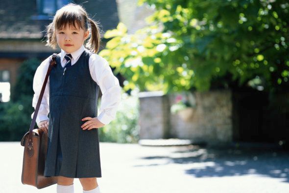 Girl (3-5) wearing school uniform, holding bag, outdoors, portrait