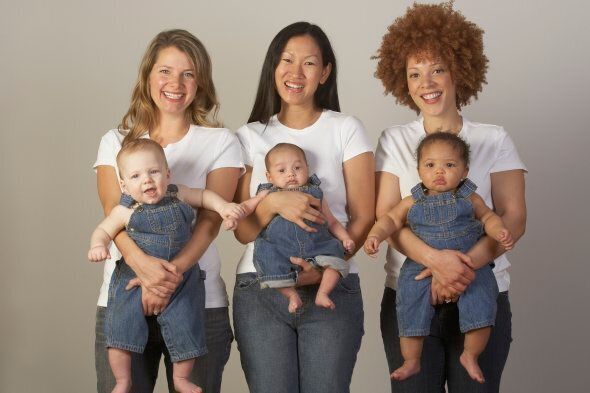 Three young mothers holding babies in overalls