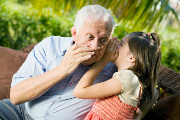 Close-up of a girl whispering into her grandfather's ear