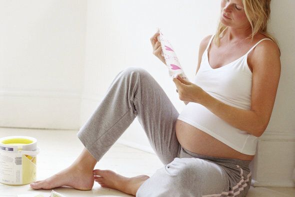 Pregnant woman on floor by paint pots, looking at fabric samples