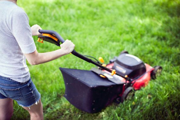 A low angle view of a young woman mowing the lawn with a mower, the grass glowing a vibrant green. Horizontal with copy space.
