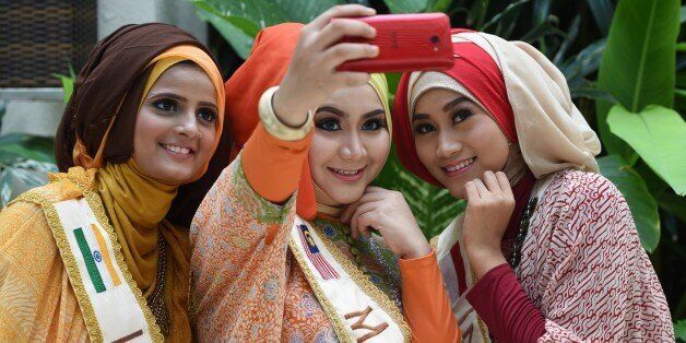 From L-R: Nazreen of India, Nur Khairunnisa of Malaysia, and Lulu Susanti of Indonesia, three of the finalists in the World Muslimah Awards, pose for a selfie as they wear Indonesian handmade 'batik' creations from the Danar Hadi collection in Yogyakarta on November 20, 2014. Indonesia is hosting the 4th World Muslimah Awards beauty pageant, exclusive to Muslim women, in Yogyakarta from November 13-21. AFP PHOTO / ADEK BERRY (Photo credit should read ADEK BERRY/AFP/Getty Images)
