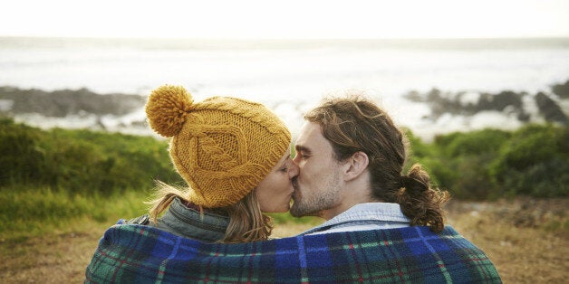 Rearview shot of an affectionate young couple wrapped in a blanket at their campsite