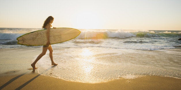 Mixed race woman carrying surfboard on beach