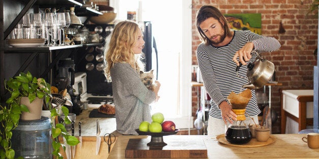 young couple making morning coffee in their kitchen while woman cradles small dog