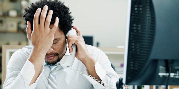 Businessman on phone at desk in office with hand on forehead