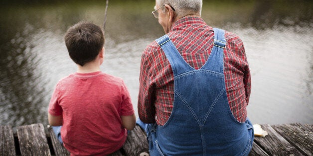 Color image of a young boy fishing with his grandfather while sitting on a dock.