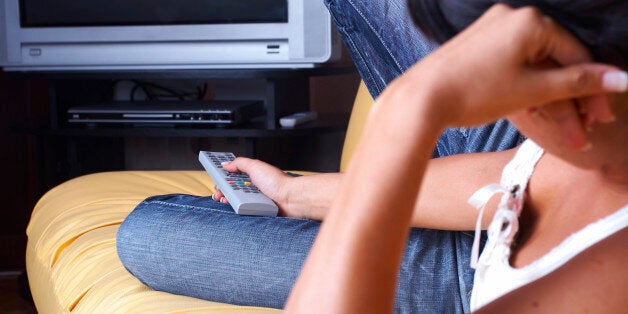 Back view on woman lying in bed and changing TV channels with remote (focus on remote controller)