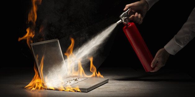 Businessman using fire extinguisher on laptop computer that is in flames