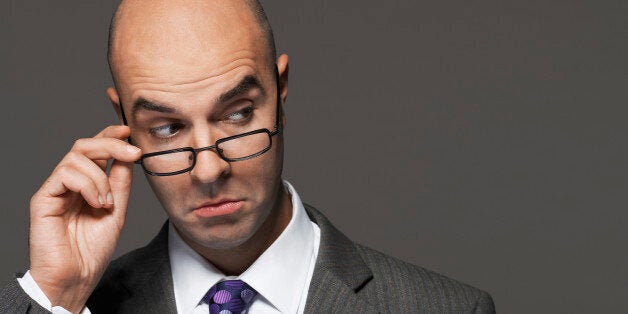 Closeup of a businessman with hand on glasses making a face against gray background