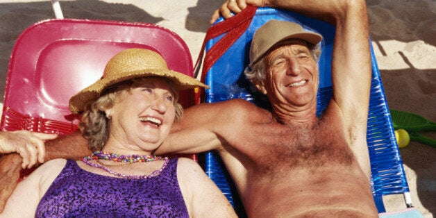 Senior couple lying on sun beds on beach, smiling