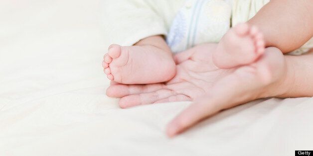 Mother's hands holding newborn's feet on bed