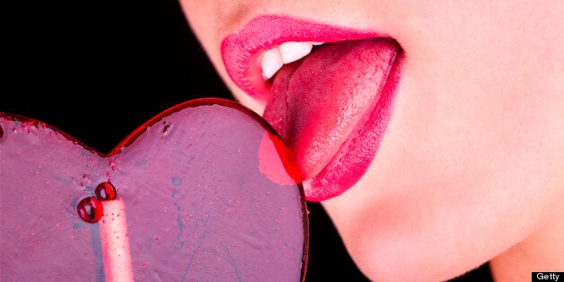 Girl licks heart lollipop on black background