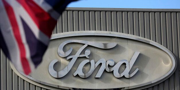 A Ford logo is seen on a stamping operations building near a Union Jack flag at the Ford Motor Co. automobile factory in Dagenham, U.K., on Monday, Oct. 29, 2012. Ford Motor Co. will shut three European plants, its first factory closings in the region in a decade, and cut 5,700 jobs to stem losses that the carmaker predicts will total more than $3 billion over two years. Photographer: Simon Dawson/Bloomberg via Getty Images